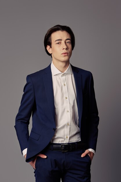 Portrait young man in navy suit over gray wall