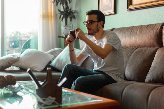 Portrait of young man playing video game holding wireless controller in his home. 