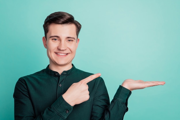 Portrait of young man point finger new product show copy spase on palm on turquoise background