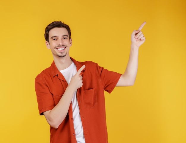 Photo portrait of young man pointing fingers at copy space isolated on yellow studio background