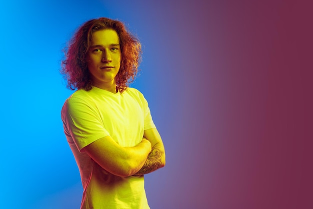 Portrait of young man posing looking at camera isolated over gradient purple blue background in neon light