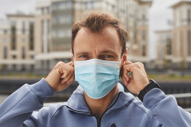 Portrait of young man in protective mask looking at camera while walking in the city