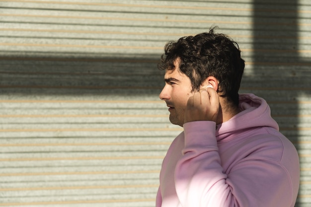 Portrait of young man putting on wireless headset for sports, wears pink sweatshirt