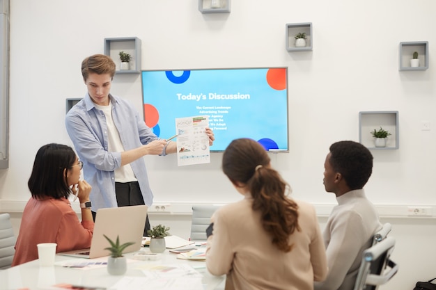 Portrait of young man showing data graphs while giving presentation during meeting in office