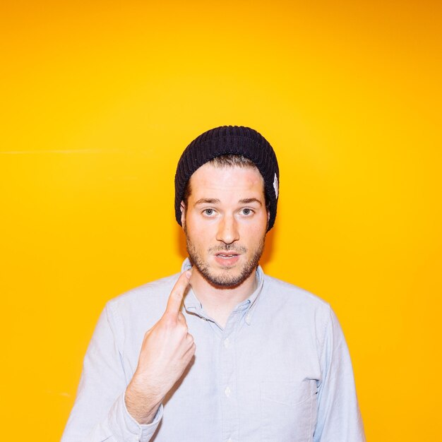 Portrait of young man showing index finger against yellow background