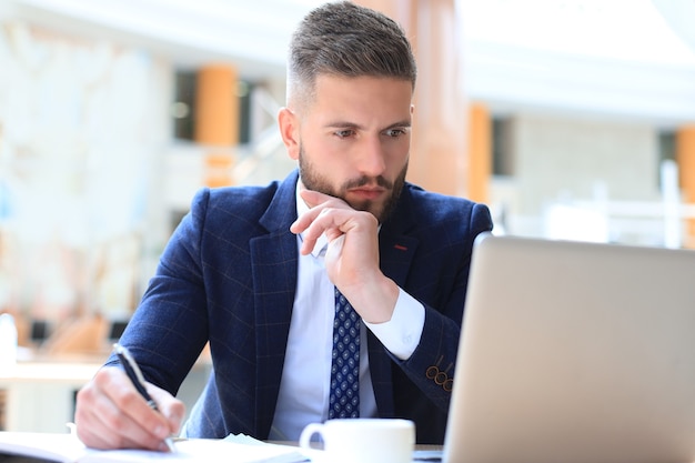 Foto ritratto di giovane uomo seduto alla sua scrivania in ufficio.