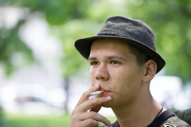 Portrait of young man smoking cigarette in summer park close up