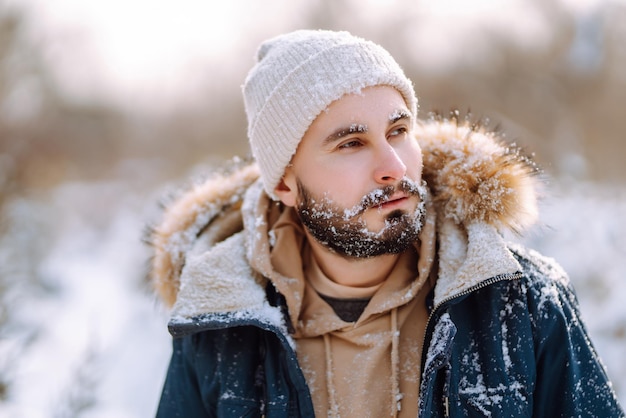 Portrait of young man in snowy winter forest Season christmas travel and people concept