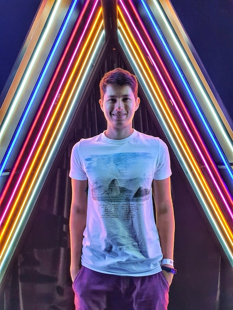 Portrait of young man standing against illuminated light trails rainbow