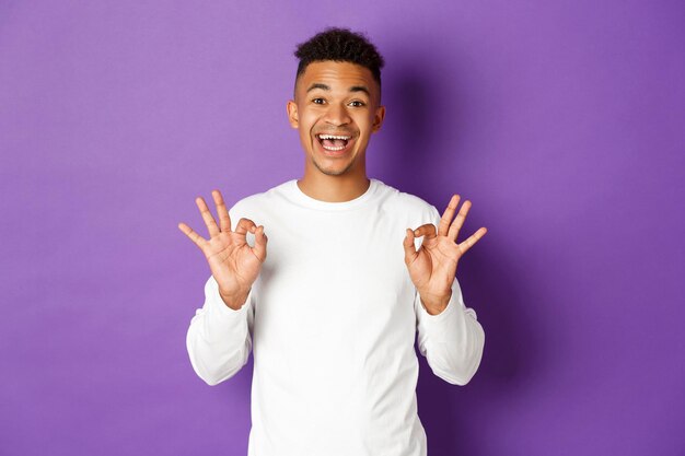 Portrait of young man standing against purple background