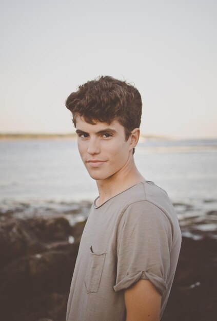 Portrait of young man standing by sea against clear sky