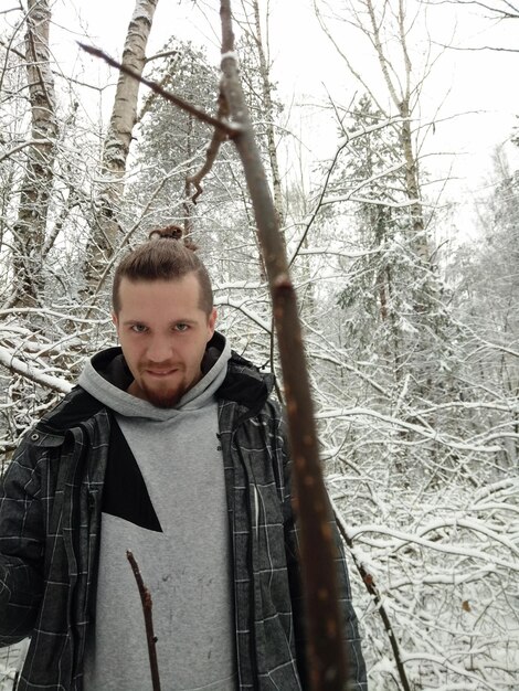 Portrait of young man standing in forest during winter