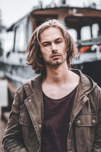 Photo portrait of young man standing in front of a boat looking at camera