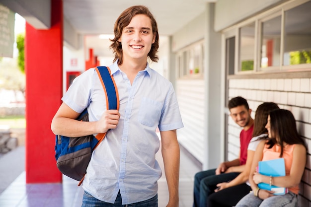 Portrait of a young man standing in a university hallway and smiling next to some of his friends