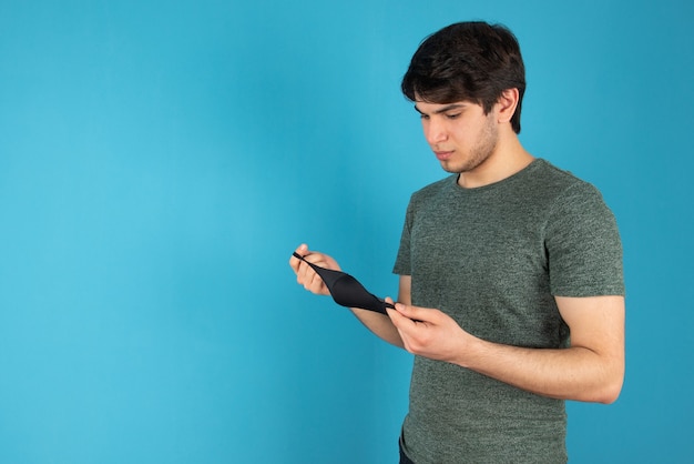 Portrait of a young man standing with black medical mask against blue.