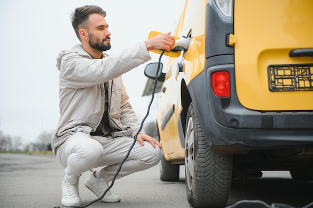 Portrait of a young man standing with charging cable near the charging station