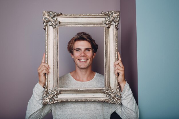 Portrait young man standing with picture frame at studio