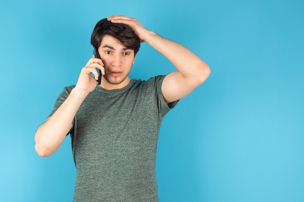 Portrait of a young man talking on mobile phone against blue.