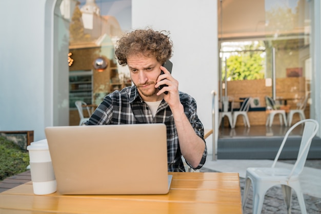 Portrait of young man talking on the phone while sitting in a coffee shop. Communication concept.