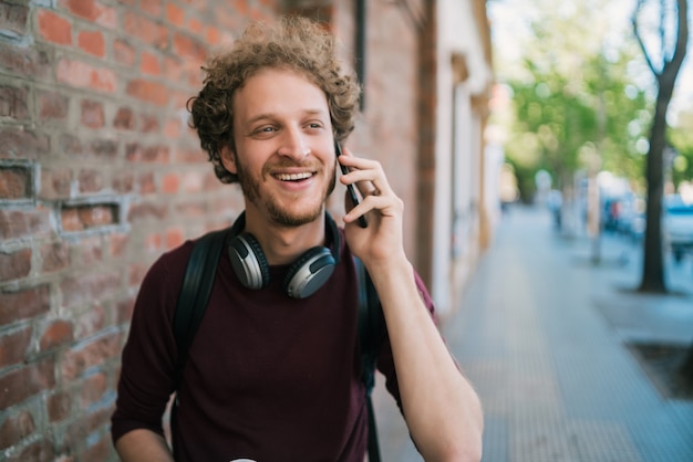 Ritratto di giovane uomo che parla al telefono mentre si cammina all'aperto in strada. comunicazione e concetto urbano.