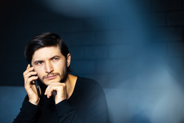 Portrait of young man, talking on the smartphone. Background of black brick wall. Copy space concept.