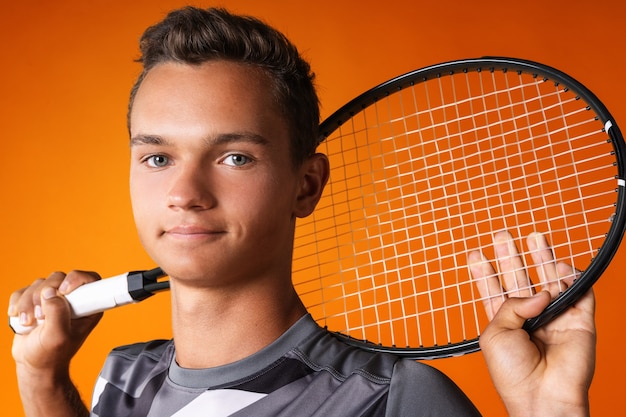 Portrait of a young man tennis player on orange background