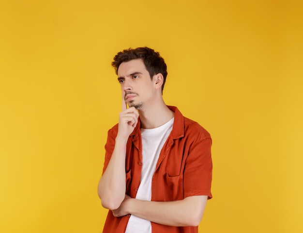 Portrait of young man thinking touching chin isolated over yellow background