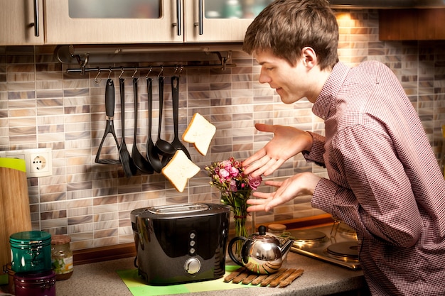 Photo portrait of young man trying to catch toasts popping out of toaster