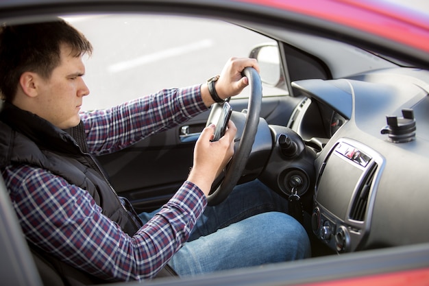 Foto ritratto di giovane uomo che scrive un messaggio mentre si guida un'auto