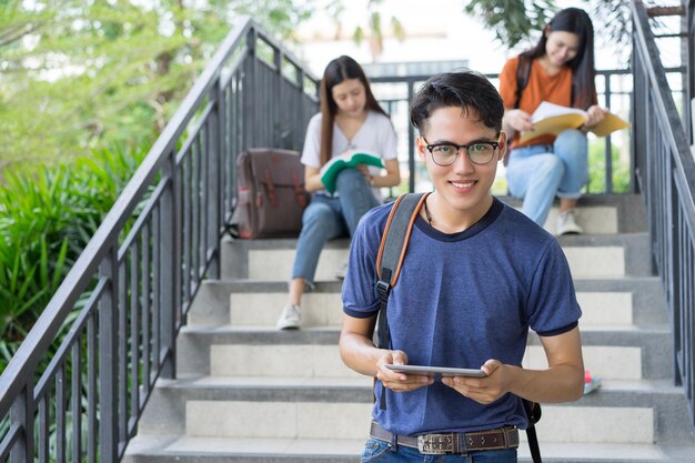 女性の友人が背景で勉強している間デジタルタブレットを使用している若者の肖像画