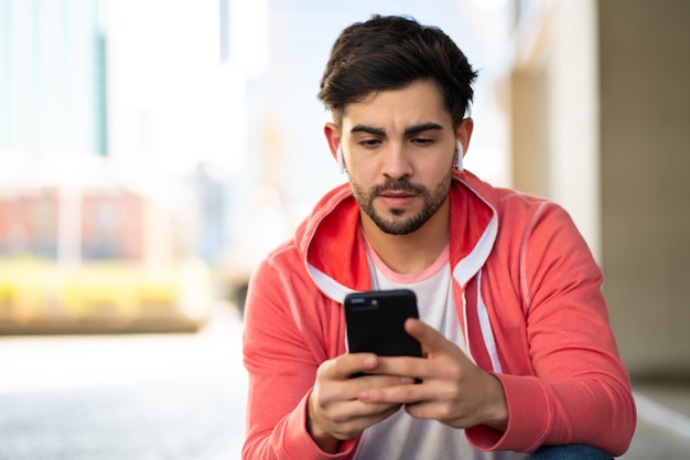 通りで屋外に座っている間彼の携帯電話を使用して若い男の肖像画。アーバンコンセプト。