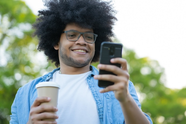 Ritratto di giovane uomo utilizzando il suo telefono cellulare in piedi all'aperto sulla strada