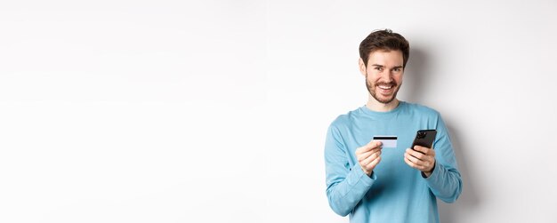 Portrait of young man using mobile phone while standing against white background