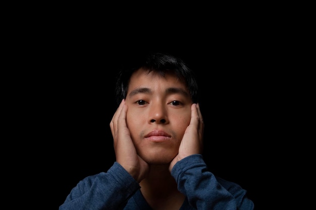 Portrait of a young man wearing blue tshirt touching cheek by hand looking at camera studio shot on black background copy space