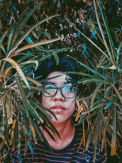 Photo portrait of young man wearing eyeglasses amidst plants