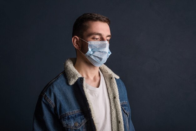 Portrait of a young man wearing a medical mask on a dark gray surface