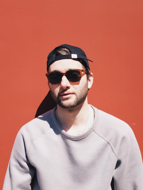 portrait of young man wearing sunglasses against red background