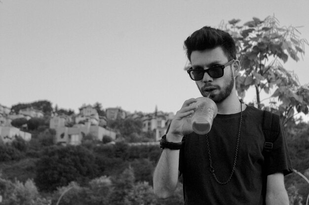 Portrait of young man wearing sunglasses standing against sky