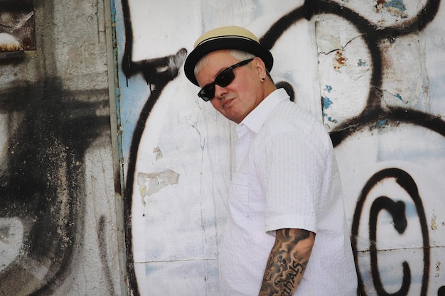 Photo portrait of young man wearing sunglasses standing against wall