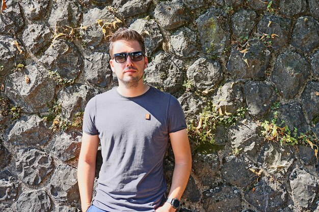 Photo portrait of young man wearing sunglasses while standing against stone wall