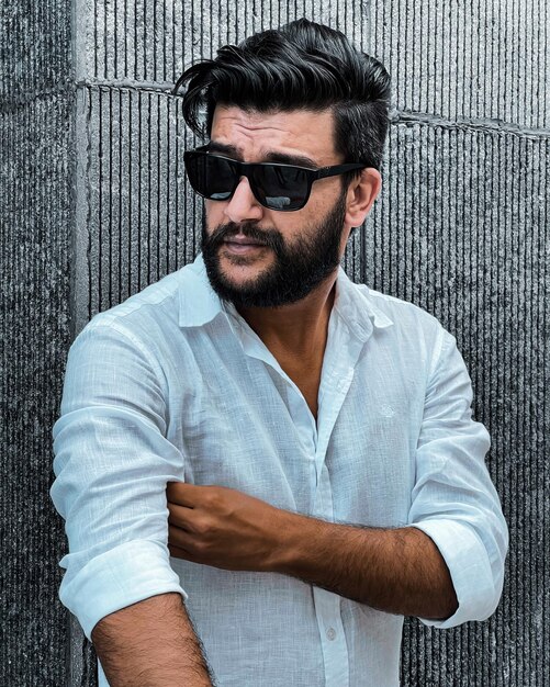 Photo portrait of young man wearing sunglasses while standing against wall