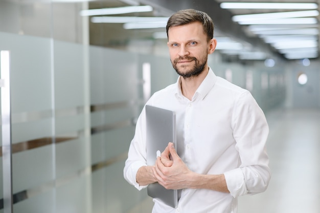 Ritratto di un giovane con una camicia bianca in ufficio il manager in ufficio tiene in mano una foto di alta qualità del laptop