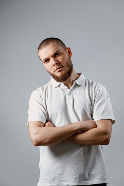 Portrait of young man in a white t-shirt seriously on gray