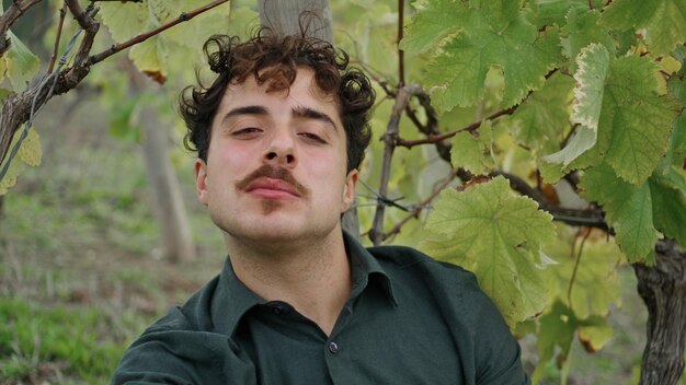 Portrait young man winegrower sitting under vine eating grapes worker relaxing