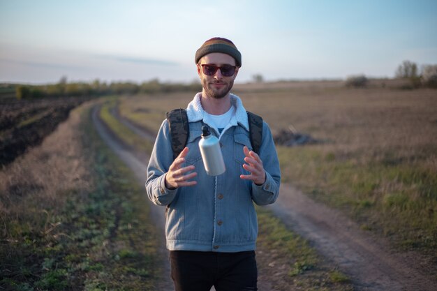 Portrait of young man with backpack holding reusable aluminum thermo water bottle in hand