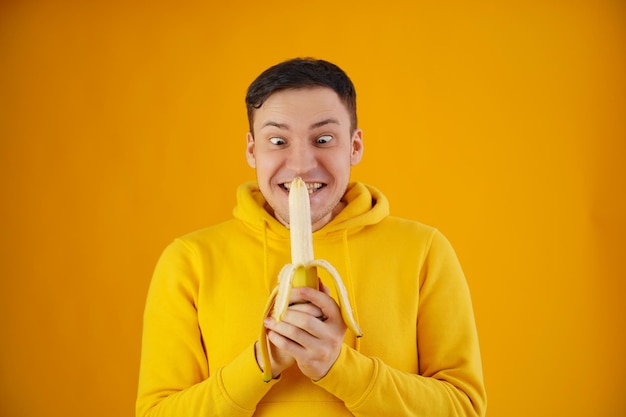 Portrait of young man with banana on yellow background Funny guy in yellow hoodie posing wth fruit