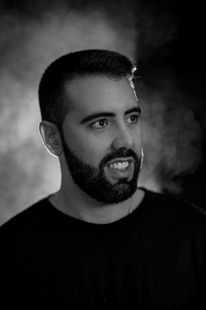 Portrait of a young man with beard in black and white on a
black background with smoke