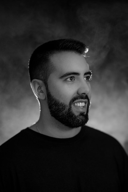 Portrait of a young man with beard in black and white on a\
black background with smoke