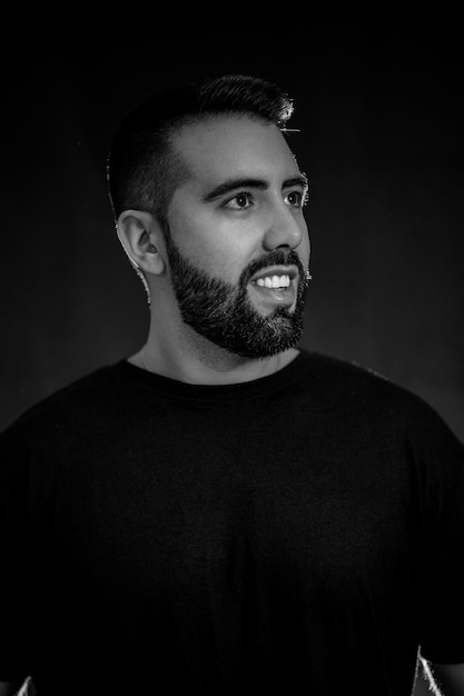 Portrait of a young man with beard in black and white on a\
black background with smoke