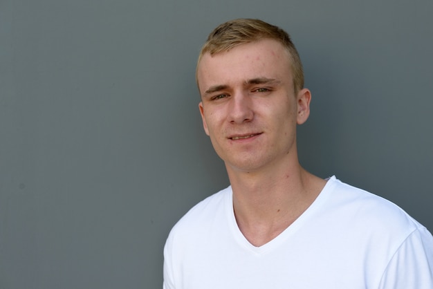 Portrait of young man with blond hair against gray concrete wall outdoors